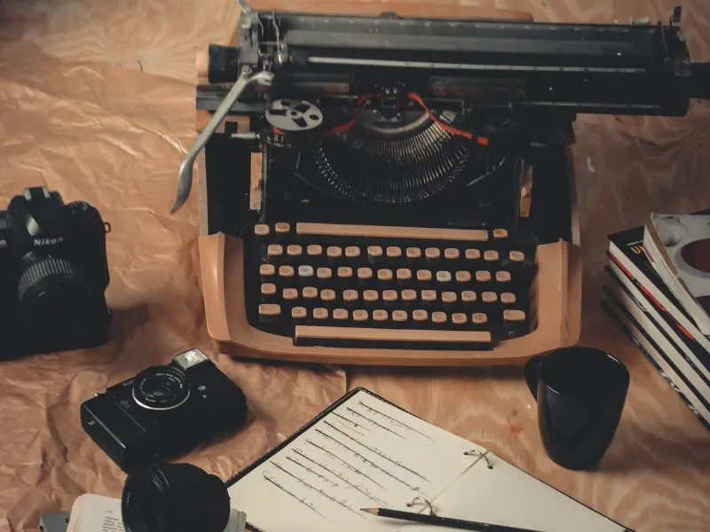 A vintage typewriter with cameras and a notebook