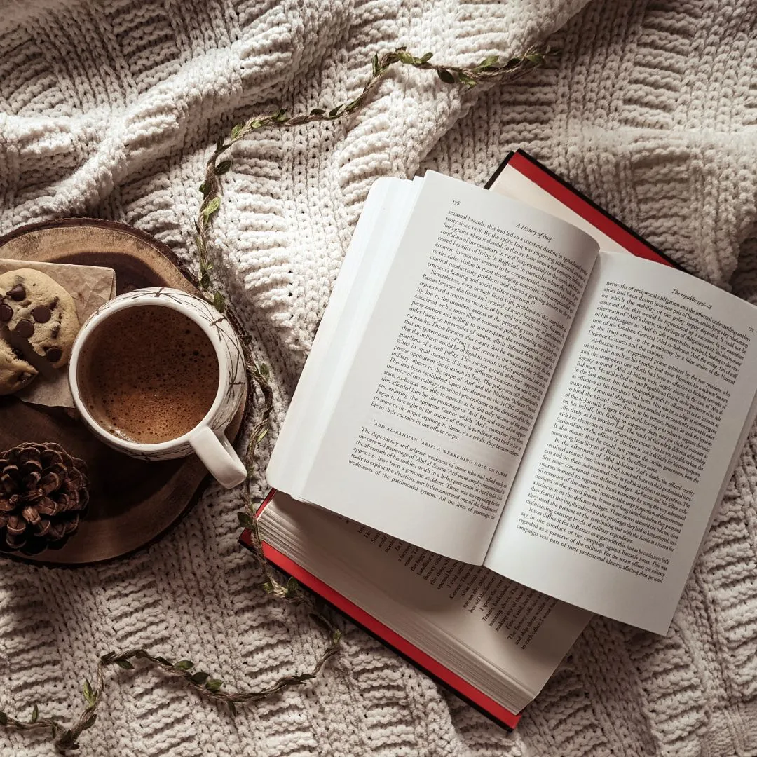 An open book and a cup of coffee on a cozy knitted blanket