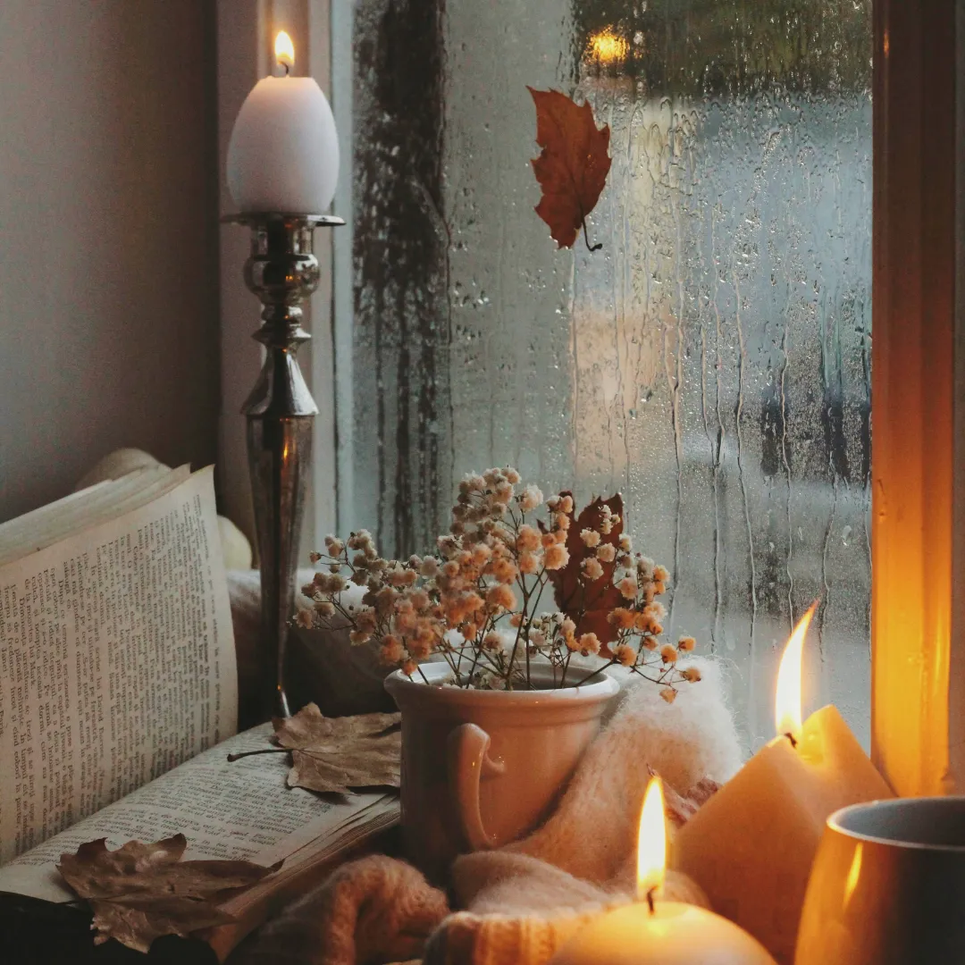 a book near a window with candle and flowers